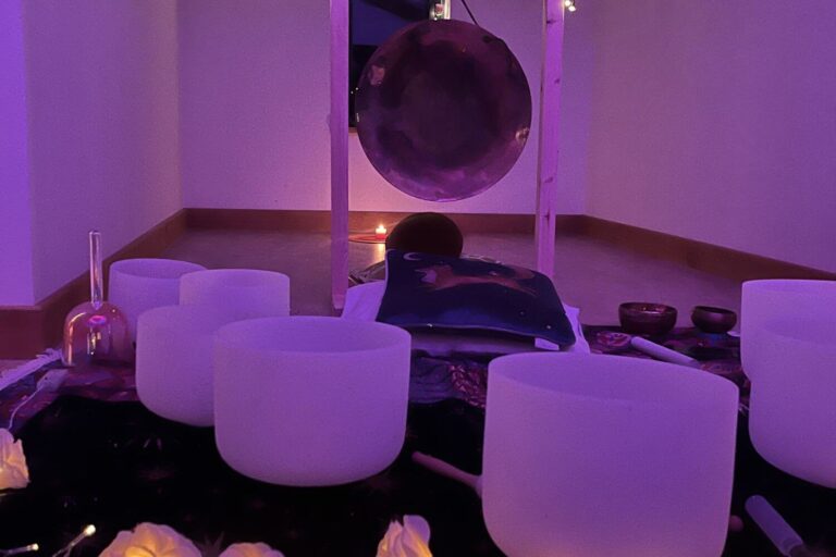 Crystal sound bowls and a gong laid out with cushions under purple lights