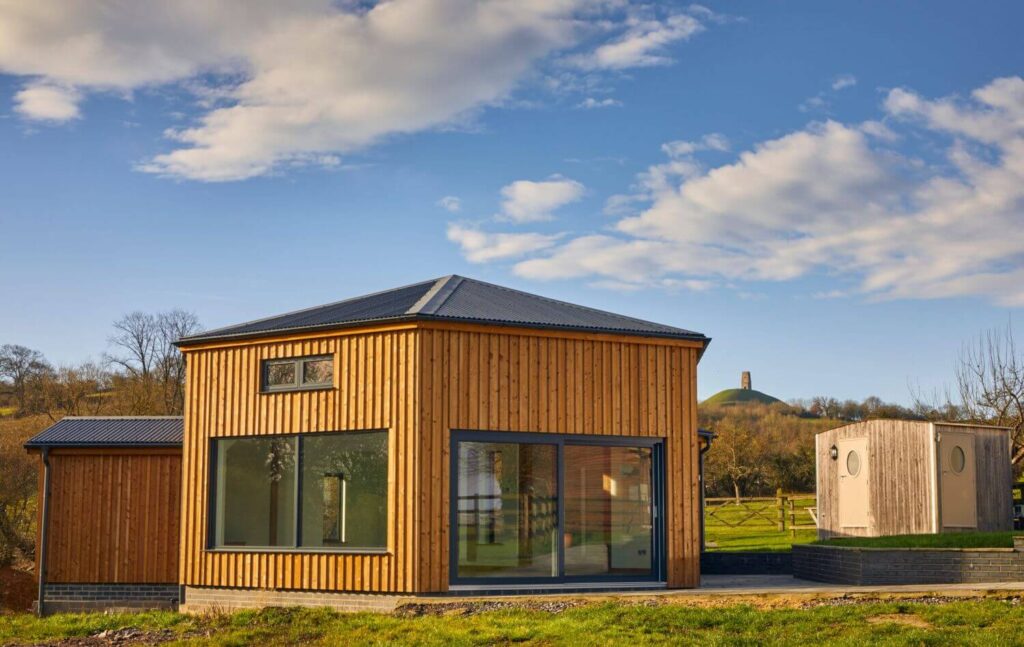 A hexagonal timber clad building with Glastonbury Tor in the background