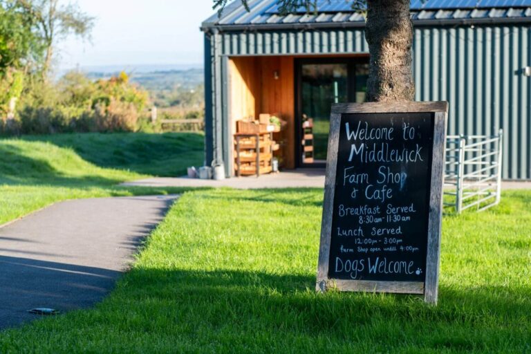 The entrance of Middlewick farm shop with a hand painted sign and an expanse of bright green grass out front
