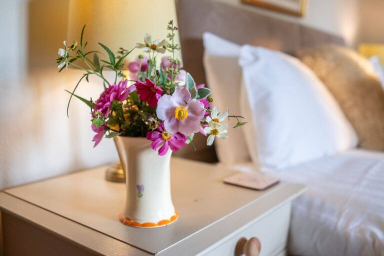 A vase of cut flowers fresh from Middlewick's gardens on a bedside table next to a king sized bread with crisp white sheets