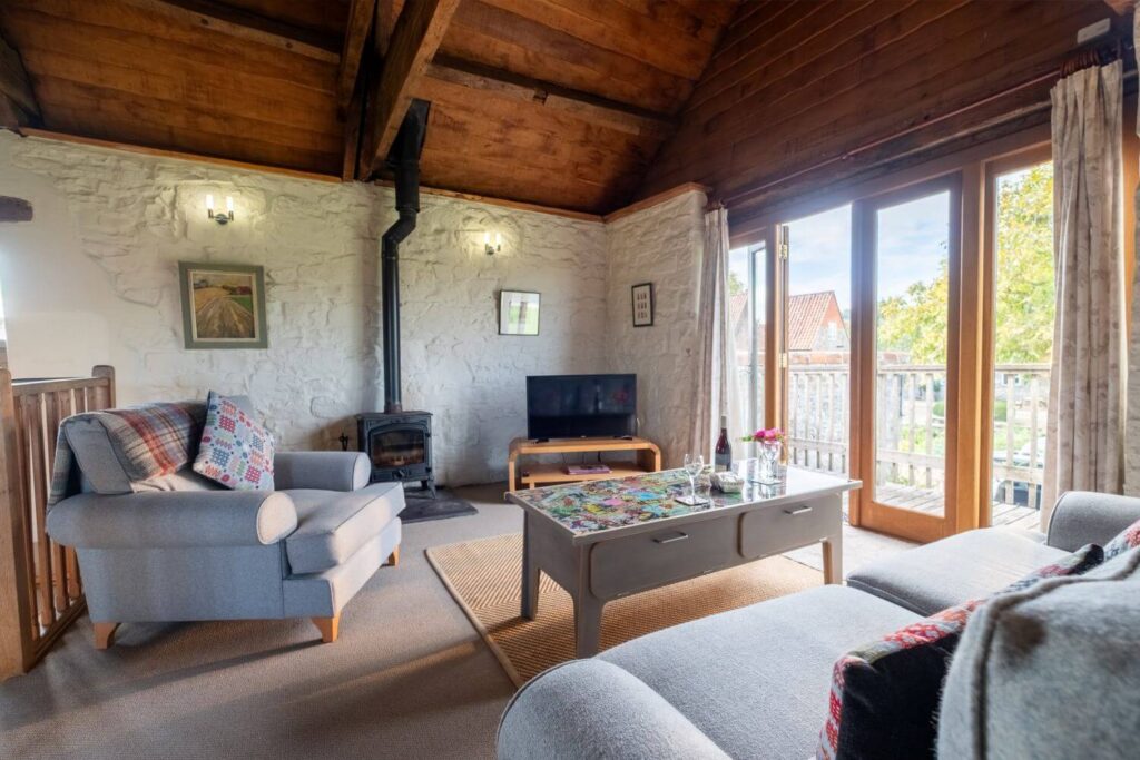 A cosy lounge with a balcony overlooking green spaces, comfy furniture and a log burner