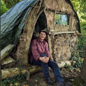 Edd Chilcott, event leader of the Middlewick Wassail, sitting in a natural structure