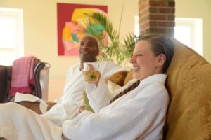 A smiling couple drinking herbal tea while wearing robes in the lounge at Middlewick Spa
